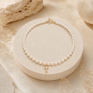Natural pearl necklace with gold-tone spacers and a cross pendant on an ivory stone display